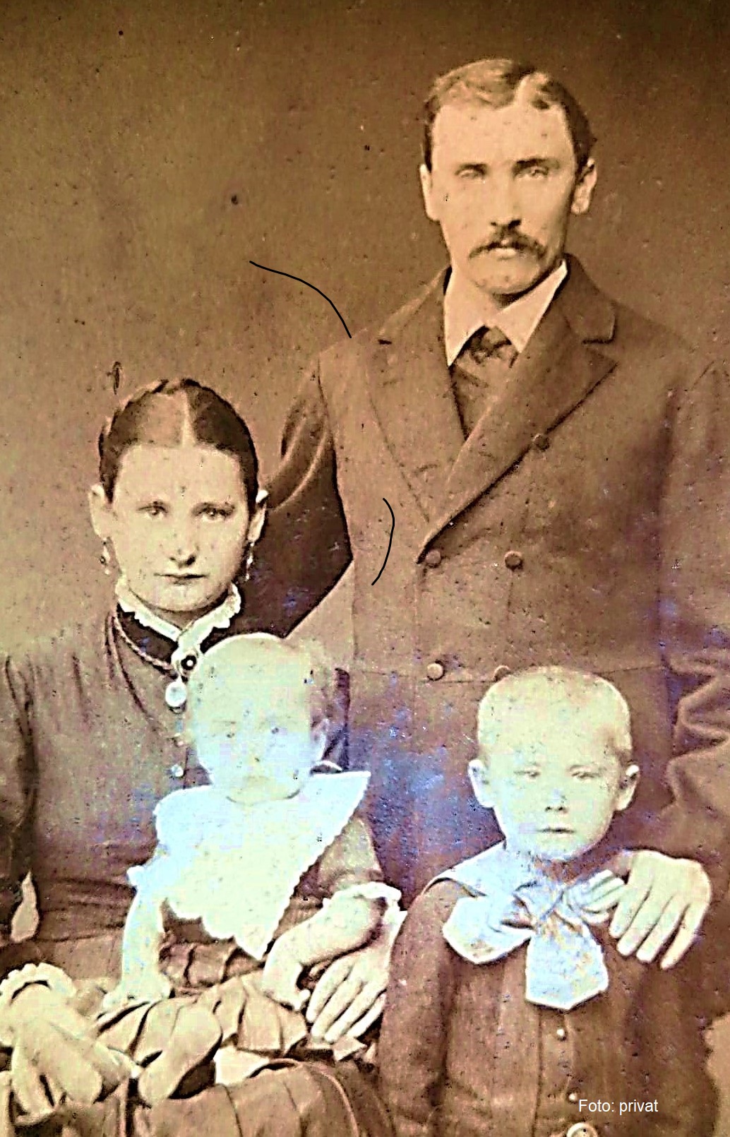 Vier Personen auf einem alten Bild. Hinten stehend ein Mann, vorne eine Frau sitzend, die ein kleines Kind hält, auf ihrem Schoss das kleine Kind, rechts von ihr ein etwas älters. Alle feierlich angezogen.