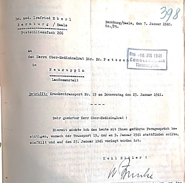 Das Foto zeigt ein altes Schreiben auf Deutsch, adressiert von "Dr. med. Irmfried Eberl" aus Bernburg/Saale an "Herrn Ober-Medizinalrat Dr. Petzsch" in Neuruppin. Datiert ist es auf den 7. Januar 1940, mit einem blauen Stempel vom 10. Januar 1941. Der Betreff nennt einen Krankentransport Nr. 19 am Donnerstag, den 23. Januar 1941. Der Briefinhalt bespricht ein Gespräch über einen Transport, der verschoben wurde. Unterschrieben ist das Schreiben mit "Heil Hitler!" und einer unleserlichen Signatur.